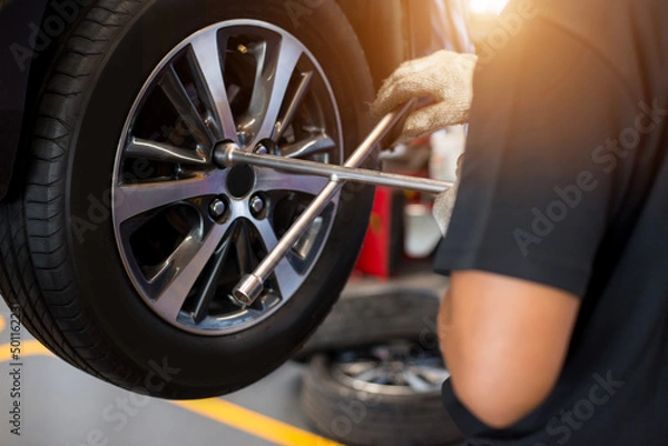 Fototapeta Auto mechanic with electric screwdriver changing tire outside at car service center. Hands replace tires on wheels. Tire installation concept.