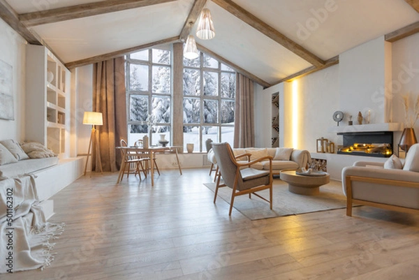 Obraz cozy warm home interior of a chic country chalet with a huge panoramic window overlooking the winter forest. open plan, wood decoration, warm colors and a family hearth