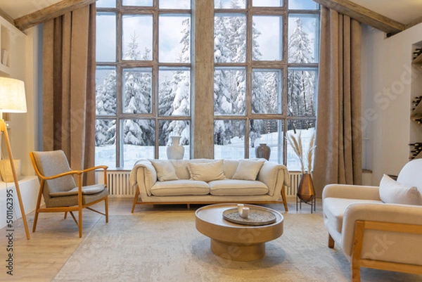 Obraz cozy warm home interior of a chic country chalet with a huge panoramic window overlooking the winter forest. open plan, wood decoration, warm colors and a family hearth
