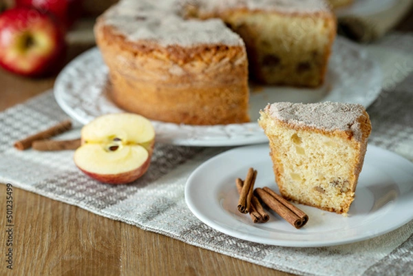 Fototapeta piece of Sponge cake or chiffon cake with apples so soft and delicious sliced ​​with ingredients: cinnamon, eggs, flour, apples on wooden table. Home bakery concept for background and wallpaper