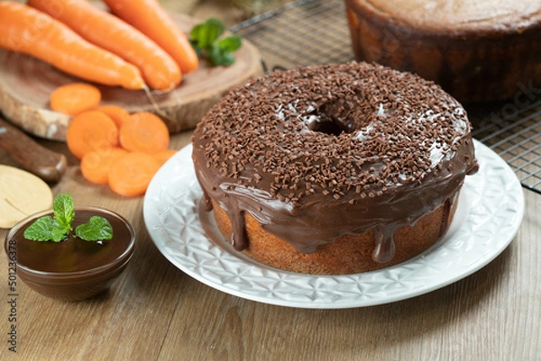 Fototapeta Brazilian carrot cake with chocolate frosting on wooden table with carrots in the background