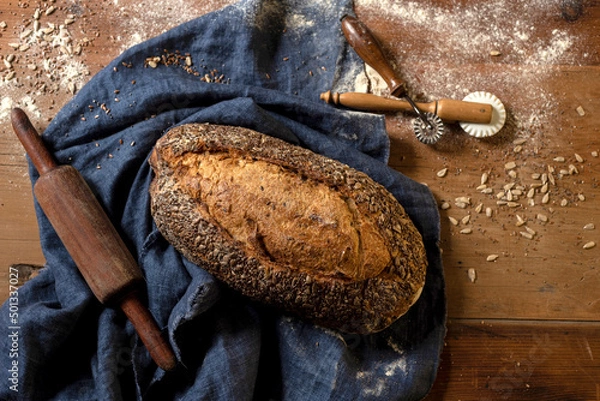 Fototapeta Homemade sourdough bread with seeds in different shapes and styles with olive oil on a still life table with a cloth rolling pin and window light