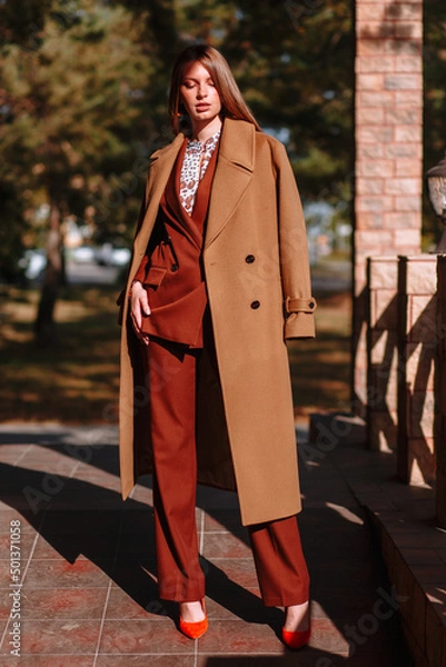 Obraz The girl is a model showing fashionable outerwear on the street, on the veranda of a summer cafe. Clothes for the showroom
