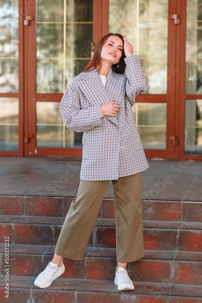 Obraz The girl is a model showing fashionable outerwear on the street, on the veranda of a summer cafe. Clothes for the showroom