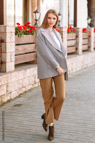 Obraz The girl is a model showing fashionable clothes on the street. Behind the girl is a cafe fence
