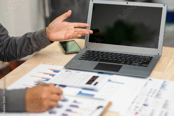 Fototapeta close up of businessman hand working on laptop computer with business graph information diagram on wooden desk as concept
