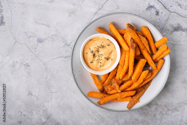 Obraz Baked sweet potato fries on a plate with savory sauce over concrete background, top view