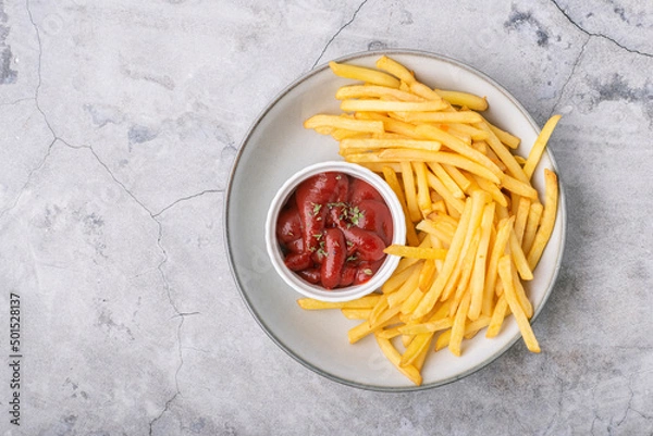 Fototapeta French fries with ketchup on a plate over concrete background, top view