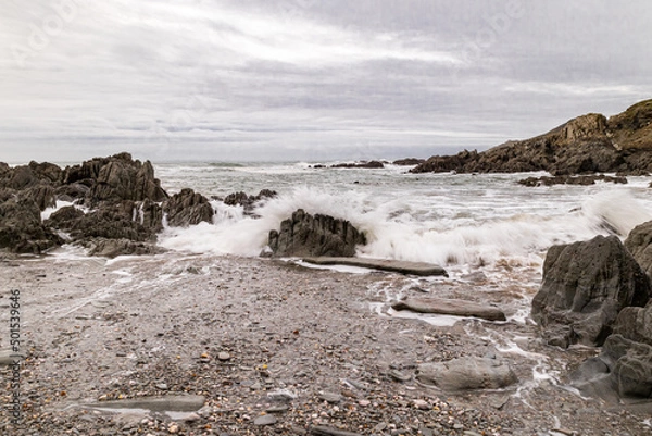 Obraz A waves hits a rock on an atmospheric North Devon beach.  The sand and pebbles in the foreground still show the remnants of the last wave.