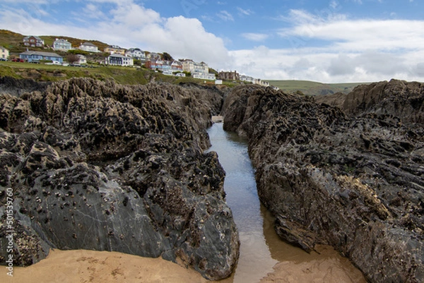 Obraz The Western edge of Woolacombe from the rocky beach below.  The rocks are covered in shell fish and a water channel leads up towards the houses on the hill.