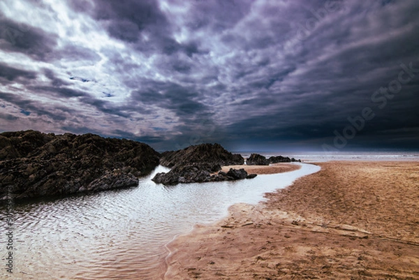 Obraz A North Devon beach between Mortehoe and Woolacombe.  Rocks, water, sand and clouds combine to bring drama.  The sun just peeks through the clouds.