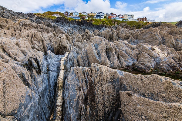 Obraz Looking up from the beach, over the rocks towards the colourful houses of Mortehoe, near Woolacombe in North Devon.  A seam of quartz seems to lead up to the village. 