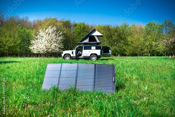 Fototapeta 4x4 Offroad vehicle camping with roof tent in a meadwow with solar panel for energy generation in foreground