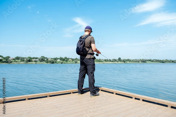 Fototapeta Fisherman with spinning rod on the lake. fisherman with spinning in his hands catching fish at sun day. Fisherman with rod, spinning reel on the river bank.