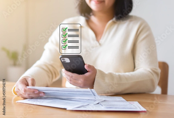 Fototapeta Expenses checklist for payment on the screen of mobile phone. Woman hands holding phone showing list of what have been paid.