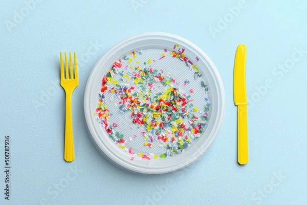 Obraz Microplastic in white plastic dish with knife and fork. Pastel blue background. Microplastic problem concept. Overhead view