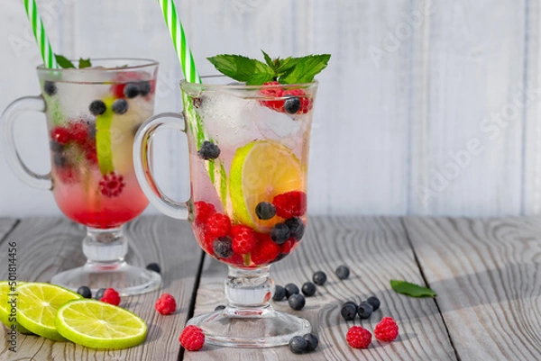 Fototapeta Fresh homemade summer cocktails with ice, lime and berries in glasses with a straw, copyspace