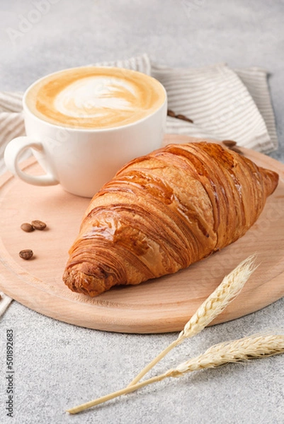 Fototapeta Large croissant and a cup of cappuccino on a light background