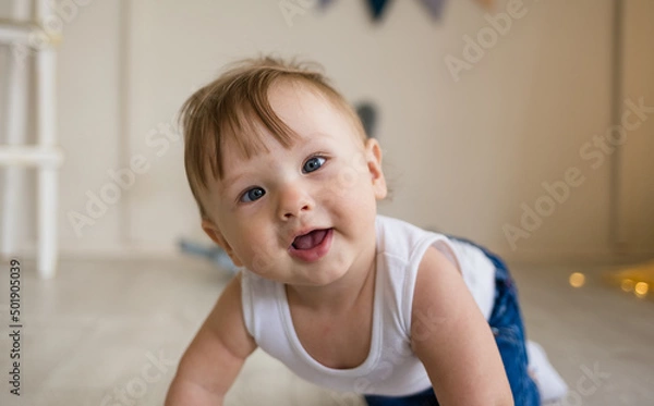Fototapeta portrait of a baby boy with a squint crawling on the floor in the nursery