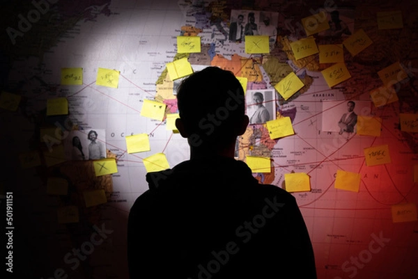 Fototapeta Silhouetted man planning in dark room. Unrecognizable man standing near wall with stickers, photographs and red threads. Planning, conspiracy concept