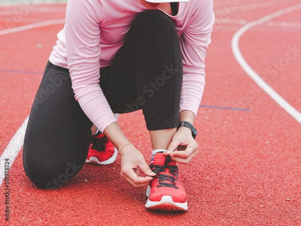 Fototapeta Running woman tying her shoelaces in preparation for a jogging run on a treadmill. for good health. The runner's concept