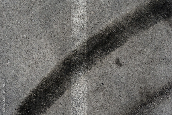 Fototapeta Asphalt texture with white line and tire marks. Smooth asphalt road. Tarmac dark grey grainy road background.Top view