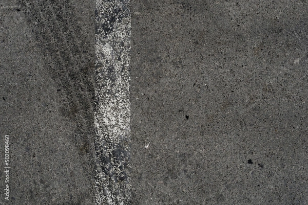 Fototapeta Asphalt texture with white line and tire marks. Smooth asphalt road. Tarmac dark grey grainy road background.Top view