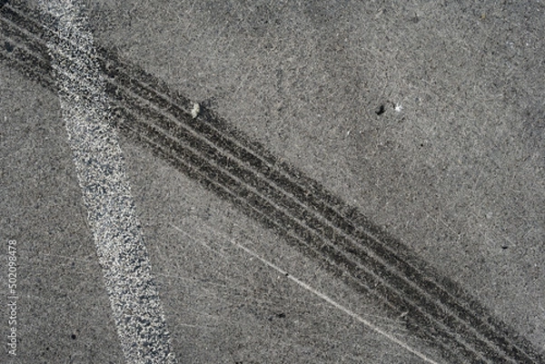 Fototapeta Asphalt texture with white line and tire marks. Smooth asphalt road. Tarmac dark grey grainy road background.Top view