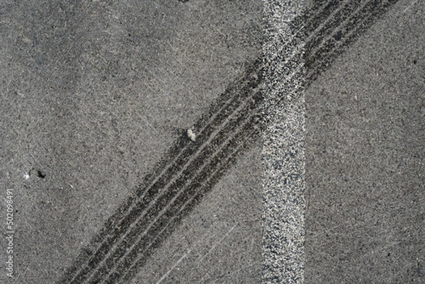Fototapeta Asphalt texture with white line and tire marks. Smooth asphalt road. Tarmac dark grey grainy road background.Top view