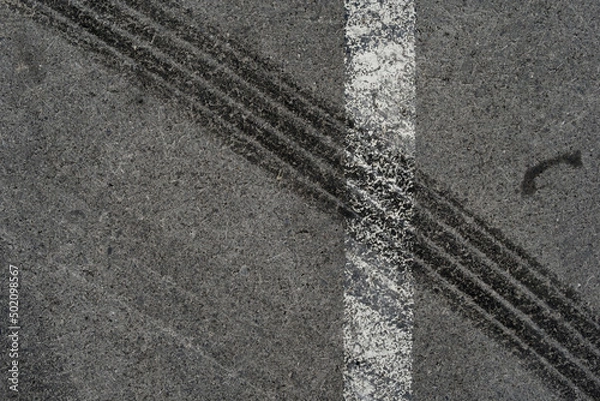 Fototapeta Asphalt texture with white line and tire marks. Smooth asphalt road. Tarmac dark grey grainy road background.Top view