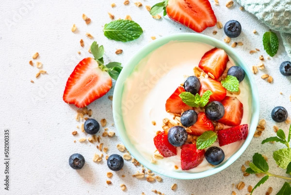 Fototapeta Greek Yogurt with granola and fresh berry mix at white stone table. Top view with copy space.