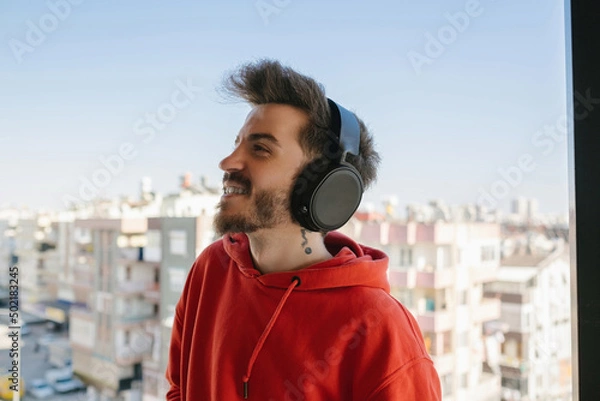 Fototapeta Headphone, man in red sweatshirt with headphones and listening to music on the balcony, listening to music and enjoying the moment