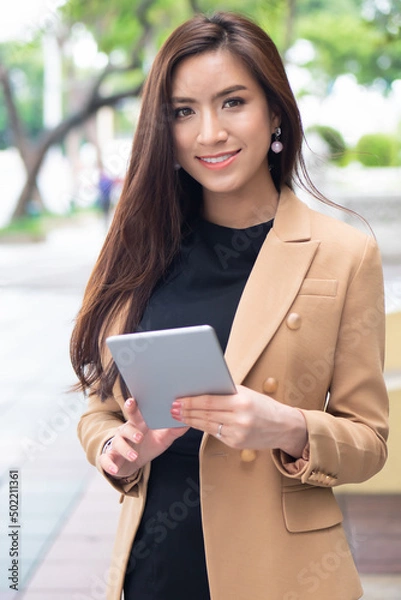 Obraz Strong working Asian business woman on duty with computer tablet in green urban street