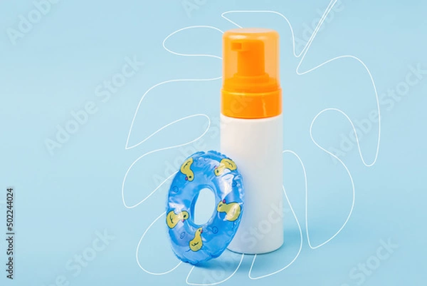 Fototapeta Blank bottle with cream after sun with decorative swimming circle near it.Hand drawing tropical leaf on background.