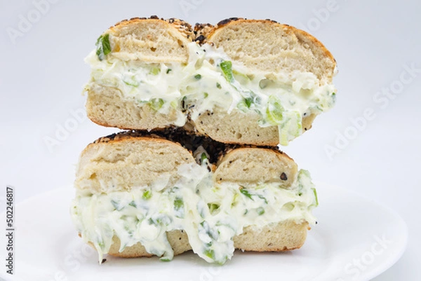 Obraz Cut in Half and Stacked New York City Style Toasted Everything Bagel filled with Scallion Cream Cheese on a White Plate