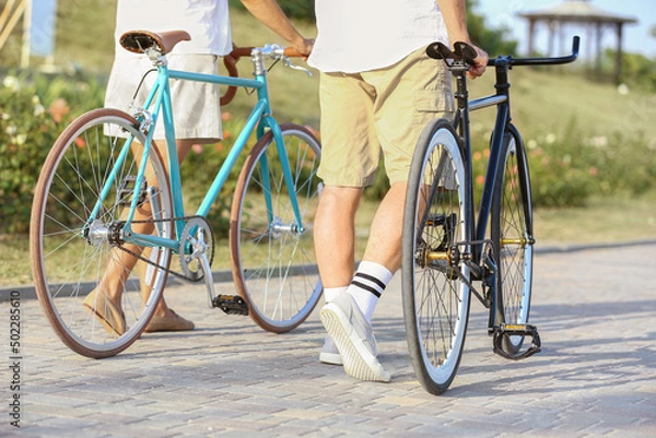 Fototapeta Mature couple with bicycles walking in city park on summer day