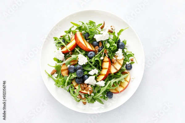 Fototapeta Peach, blueberry and arugula fresh fruit salad with cheese and almond nuts, top view