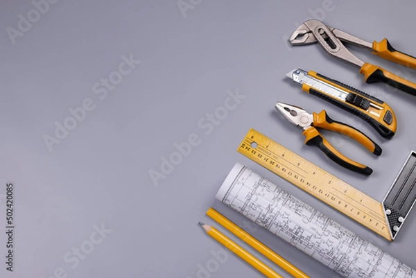 Fototapeta Project drawings roll, pencils, ruler, pliers, and other working tools on grey background. Repair and construction concept. Flat lay, top view image.