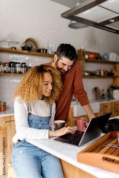 Obraz Couple looking at laptop in kitchen.