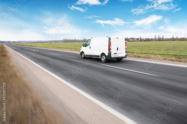 Fototapeta White van on a countryside road in motion against a sky with clouds