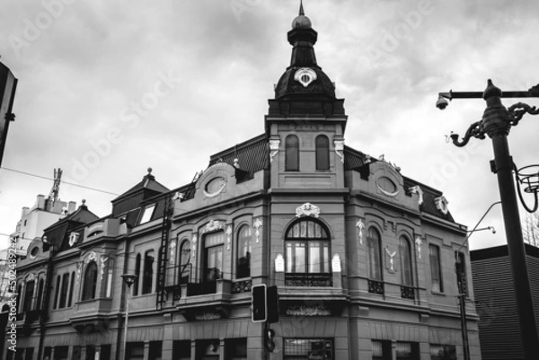 Obraz Beautiful old centuries five stored building with neoclassical architecture, ornaments, sculptures, flag and domes in a cloudy day, Valdivia, Chile (in black and white)