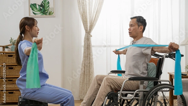 Fototapeta asian woman physiotherapist teaching handicapped older man how to use elastic band while she is doing resistance training on wheelchair at home