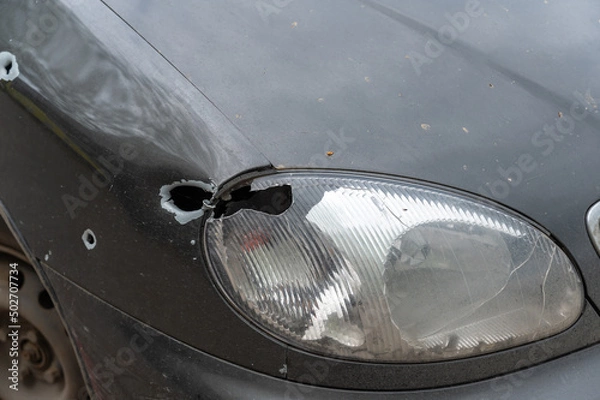 Fototapeta The front of the shot car. A sedan with a broken headlight by a bullet or shrapnel. Firing on civilians during the war between Russia and Ukraine in 2022. War crimes concept.