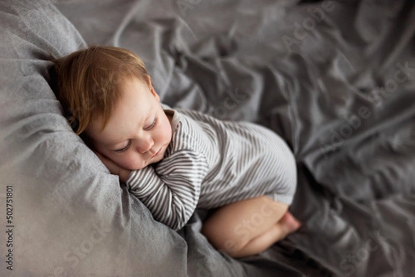 Fototapeta Mały chłopiec śpi na łóżku jak mały bobas