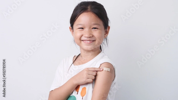 Obraz Vaccine concept. Happy Asian little child girl smiling, showing arm with plaster bandage after received, getting COVID-19 vaccine injection. Concept of inoculation, vaccinate, campaign, COVID19, Flu