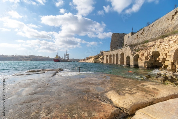 Fototapeta A slippery stone shore next to the harbor right next to Fort Ricasoli in the capital city of Malta, Valletta.
