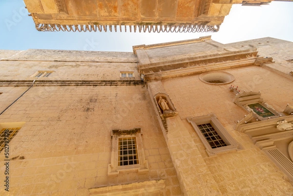 Fototapeta Old fortress buildings in narrow path with a clear sky above in old Malta Capital Mdina