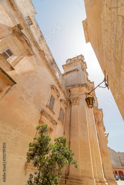 Fototapeta Sharp angled, geometric old fortress buildings with a clear sky above in old Malta Capital Mdina
