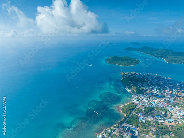 Fototapeta flying over group of the large green island and little city in the never ending blue ocean with cloudy and clear sky weather