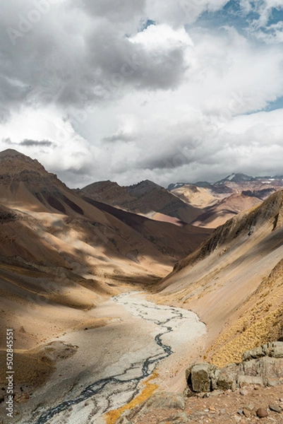 Fototapeta Vertical shot of a colorful mountain valley with a river on a sunny day with clouds, Chile